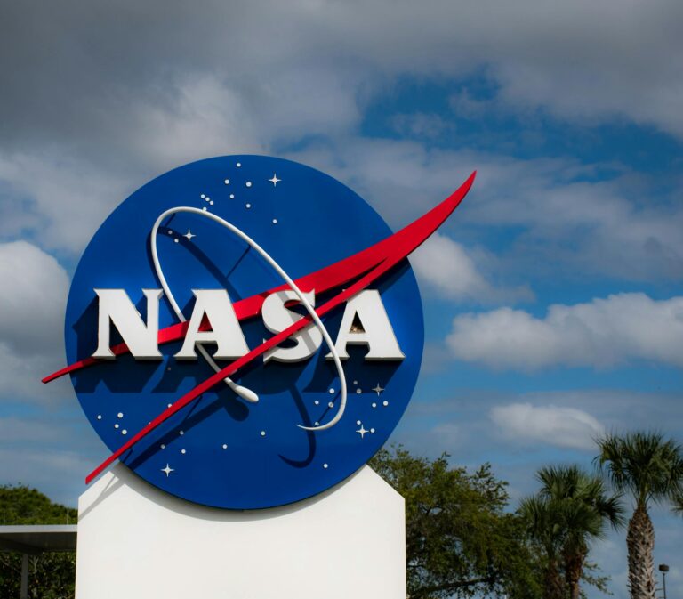 NASA's iconic logo stands prominently against a backdrop of clouds and blue sky.